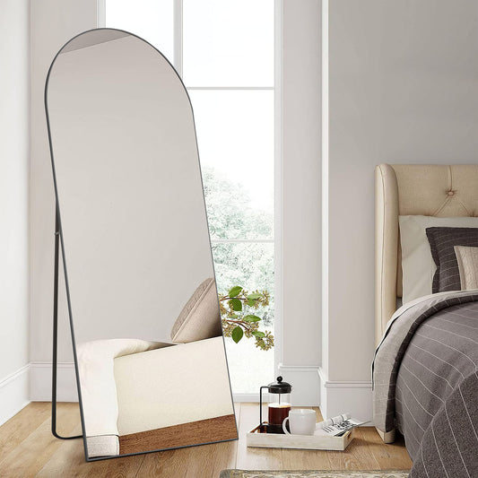 Close view of the arched floor mirror with a thin black frame and back stand in a bedroom.