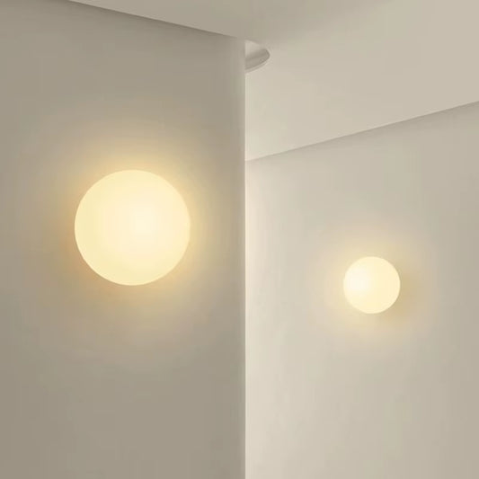 Two frosted glass globe wall lights of different sizes, lit, on a white wall.