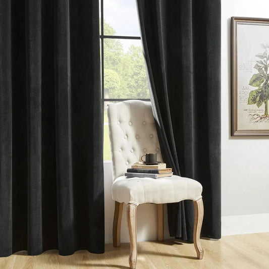 Black velvet curtain panels framing a window behind a white upholstered chair.