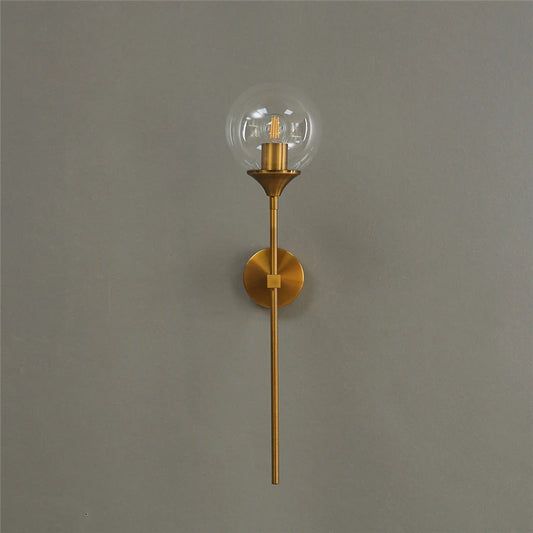 Clear glass globe wall sconce on a long gold-color metal stem, unlit, on a gray wall.