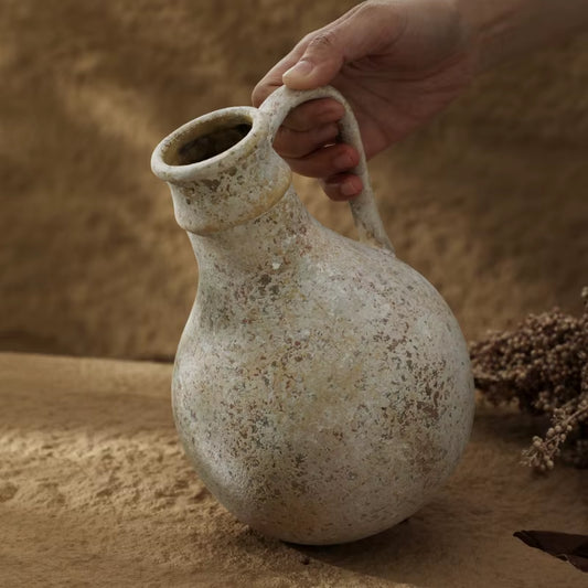 Round rustic ceramic jug vase tilted by its handle, showing the weathered grey finish.