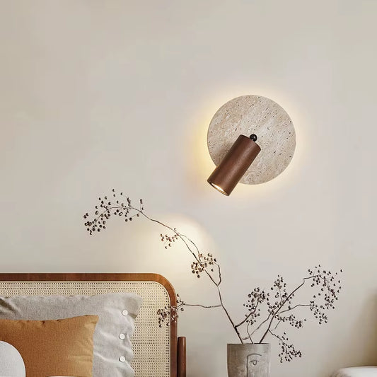 Travertine disc wall sconce lit above a bed, with a glow behind the disc