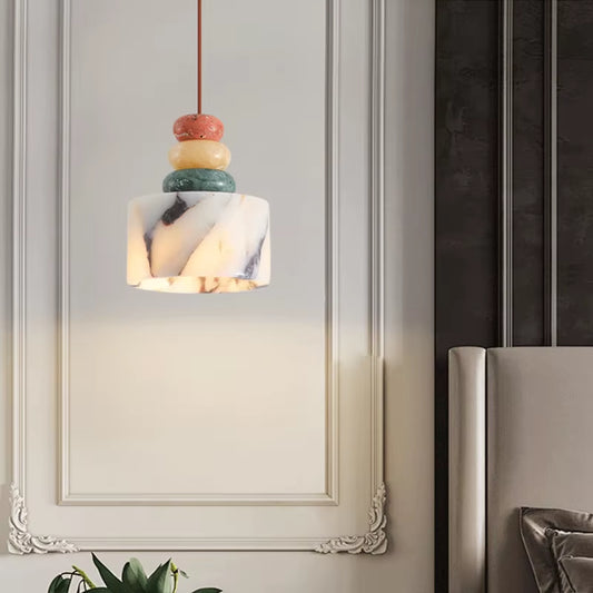 Stone drum pendant light, lit, hanging in front of a white panelled wall.