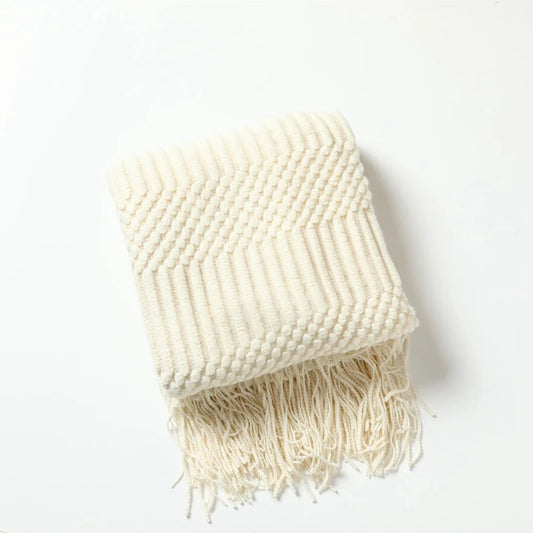 Folded cream chunky knit throw with a textured band and tassels.
