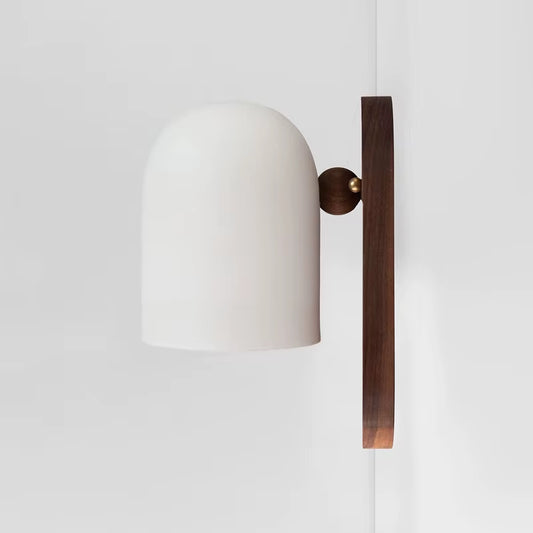 White bell shade wall sconce with an oblong walnut-color wood backplate, side view