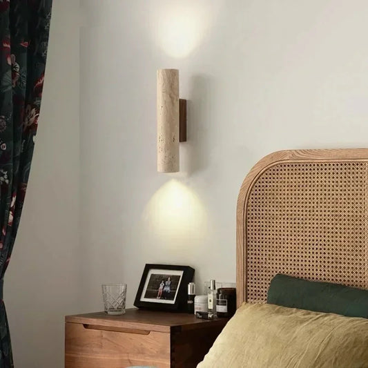 Travertine cylinder wall sconce on a walnut bracket beside a rattan headboard.