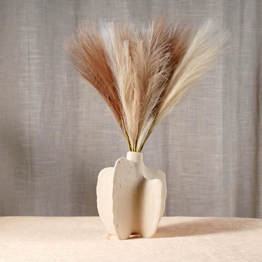 White cleft block ceramic vase holding dried pampas grass in front of a linen curtain.