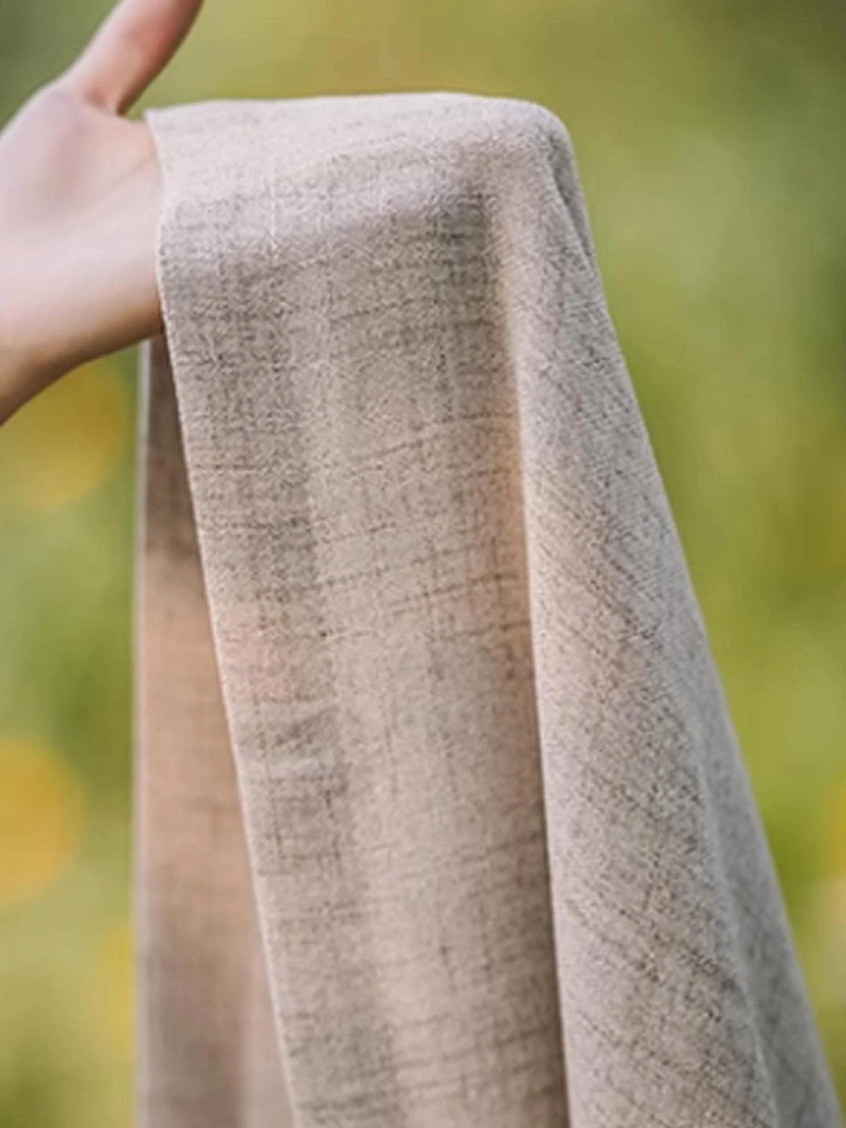 Hand holding the natural beige cotton-linen curtain fabric to show its texture.