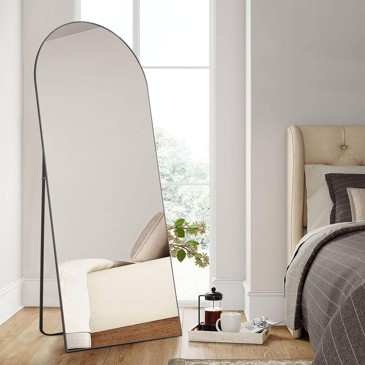 Close view of the arched floor mirror with a thin black frame and back stand in a bedroom.