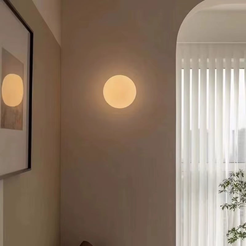 Frosted glass globe wall light, lit, on a wall beside an arched doorway.