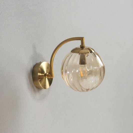 Glass wall sconce with an amber ribbed glass globe on a gold-color curved arm.