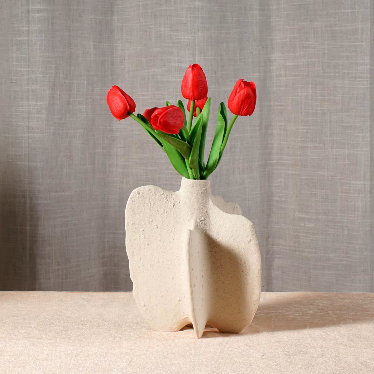 White sculptural ceramic vase seen from the side, holding red tulips.