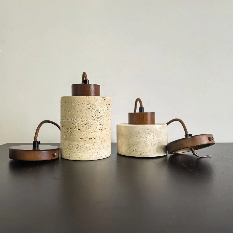 Tall and short travertine pendant shades standing on a table with their ceiling canopies.