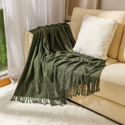 Army green chenille throw blanket with knotted fringe draped over a cream sofa.