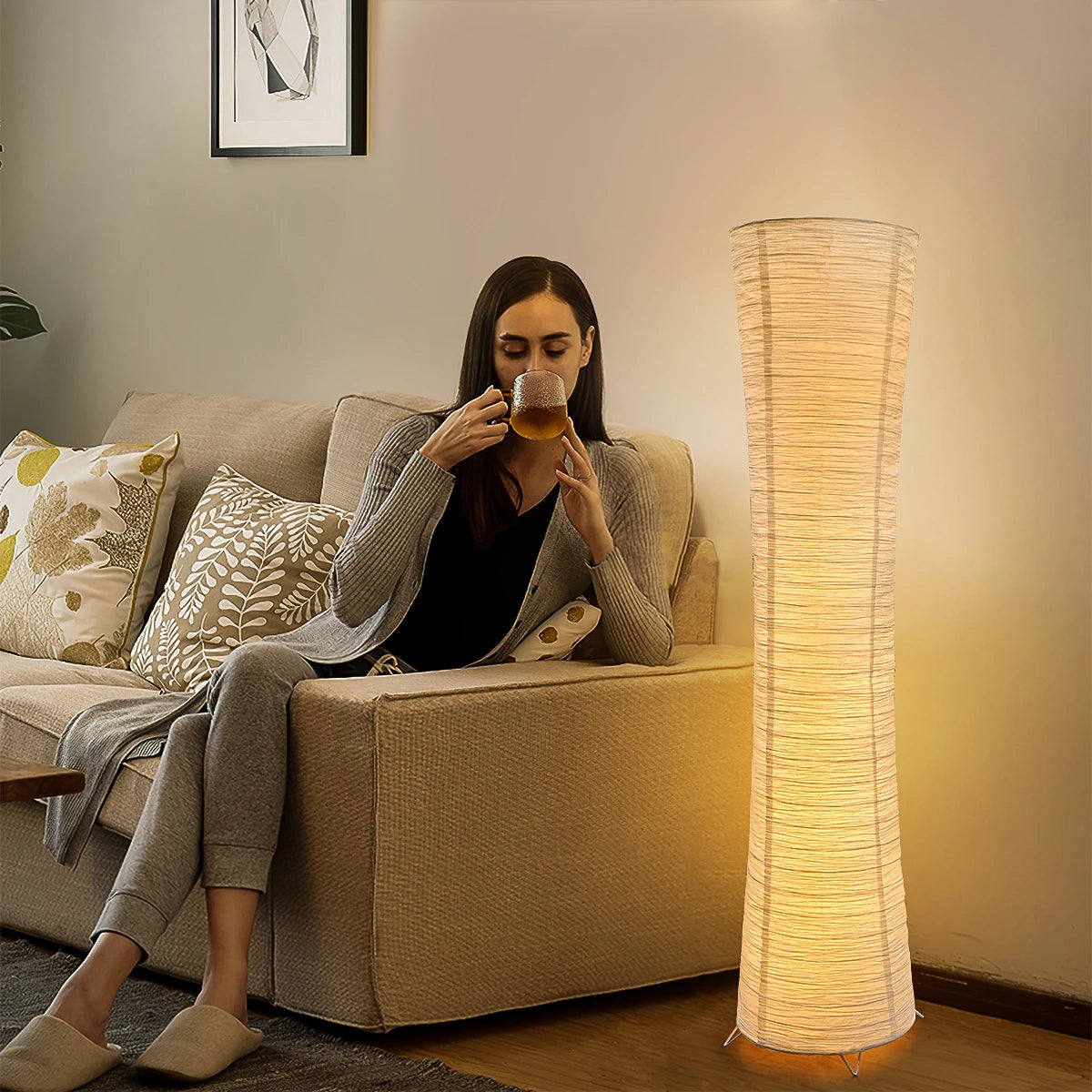 Rice paper column floor lamp giving soft light next to a sofa in the evening.