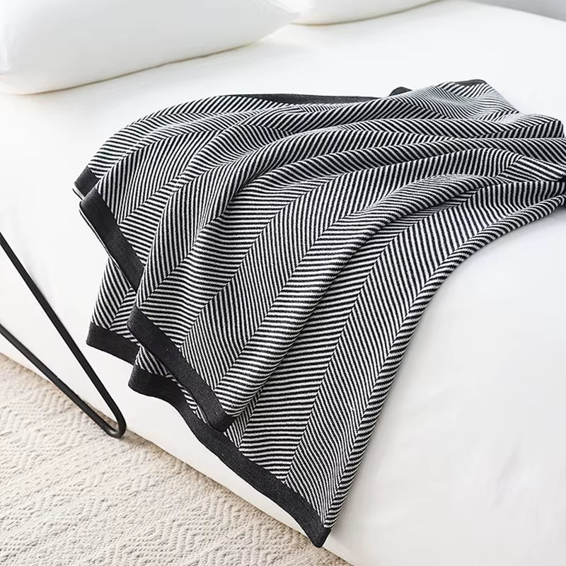 Black and white herringbone knit throw blanket draped over the end of a bed.