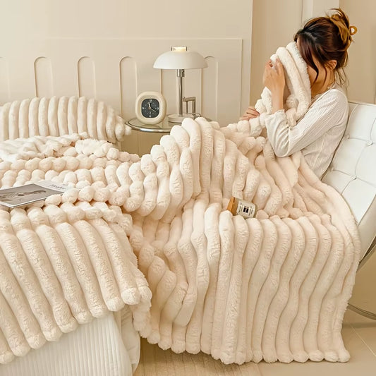 Person sitting on a bed wrapped in an ivory ribbed faux fur throw.