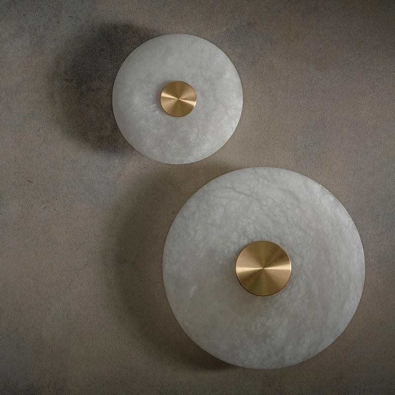 Two round marble disc wall sconces in two sizes, unlit, showing the white veined marble and metal centers.
