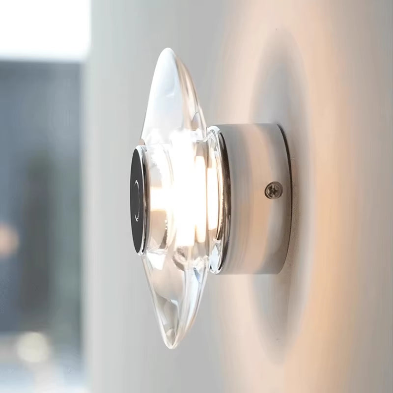 Clear crystal disc wall sconce on a chrome-color base, lit, seen from the side.