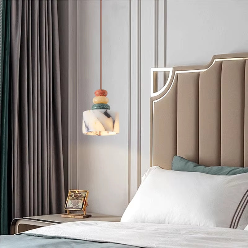 Stone drum pendant light, lit, hanging beside a bed with a tall upholstered headboard.