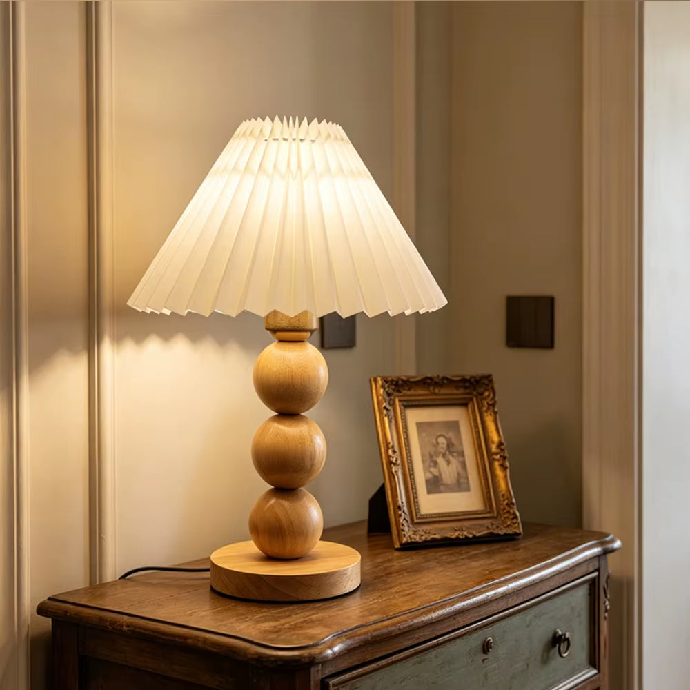 Natural wood stacked-sphere table lamp with a white pleated shade on a dark wood dresser.