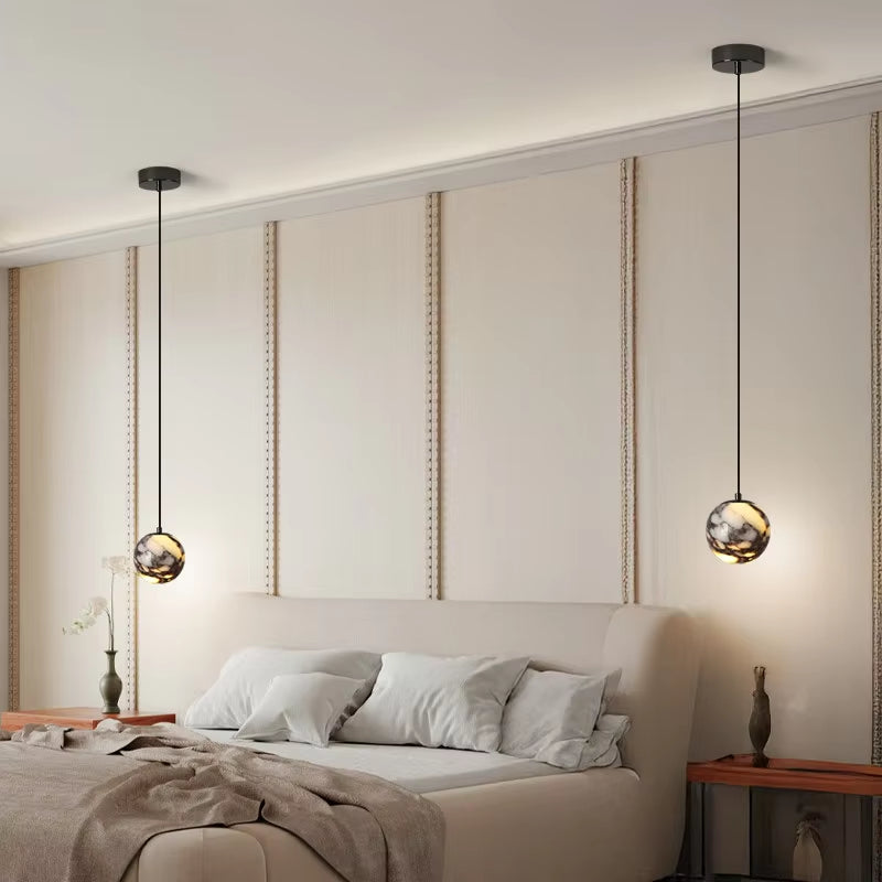 Two marble globe pendant lights, lit, hanging on either side of a bed.
