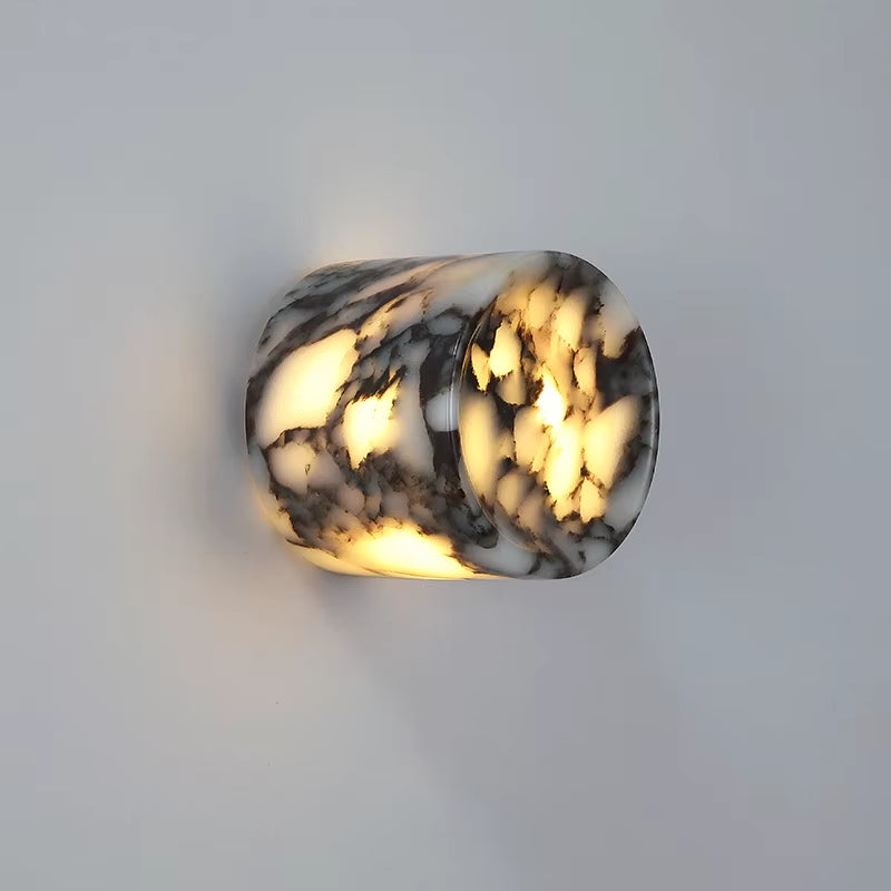 Marble cylinder wall sconce, lit, on a gray wall.