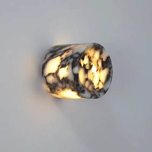 Marble cylinder wall sconce, lit, on a gray wall.