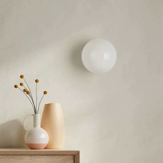 Frosted white glass globe wall light on a wall above a shelf with vases.
