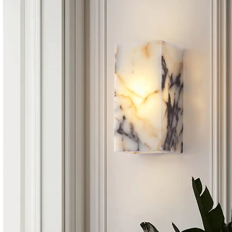 Stone block wall sconce, lit, on a panelled wall above a plant.