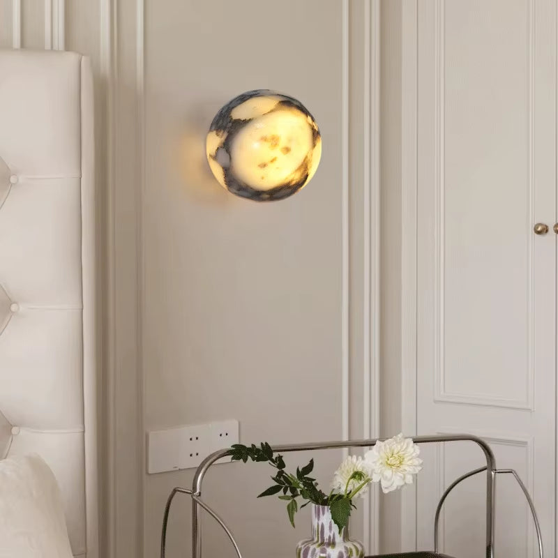 Marble sphere wall sconce, lit, on a panelled wall beside a tufted headboard.