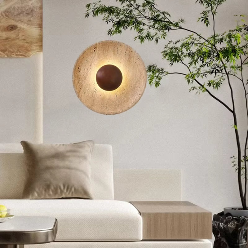 Stone disc wall sconce with a dark wood center glowing above a cream sofa in a living room.