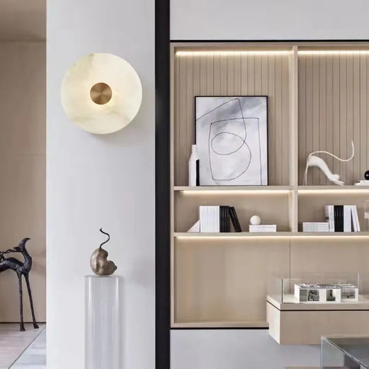 Round marble disc wall sconce with a metal center on a white wall beside open shelving.