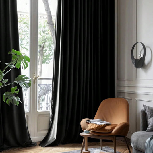 Black velvet curtain panels hanging at a tall window beside a leather armchair.
