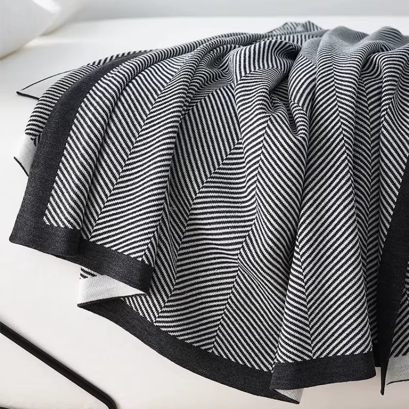 Black and white herringbone knit throw blanket with a black border, draped in folds.