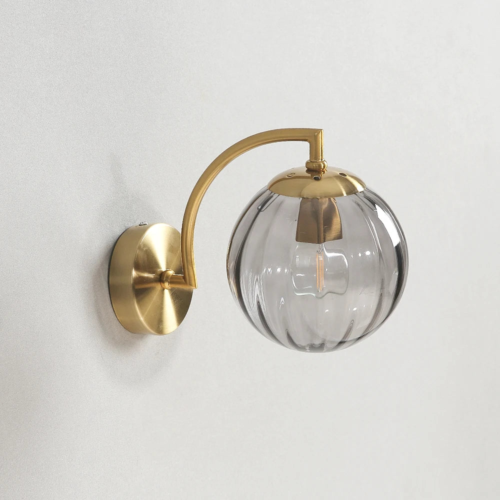 Glass wall sconce with a smoke gray ribbed glass globe on a gold-color curved arm.