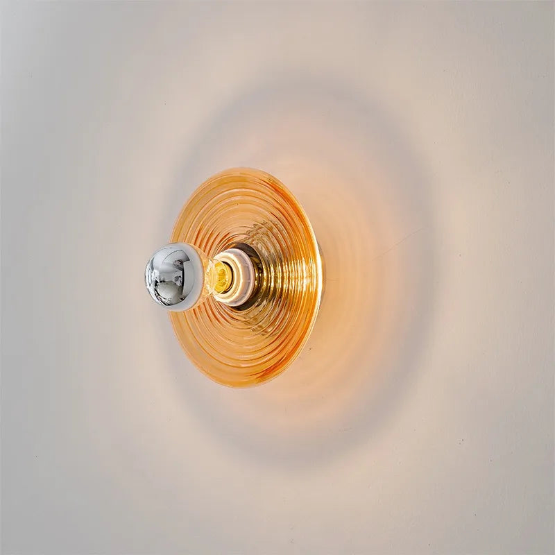 Amber ripple glass disc wall sconce, lit, on a pale wall.