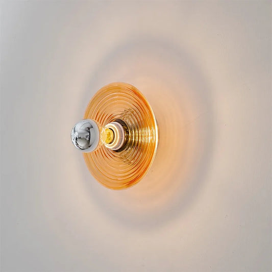 Amber ripple glass disc wall sconce, lit, on a pale wall.