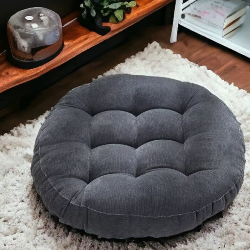 Round dark grey tufted corduroy seat cushion on a white shag rug.