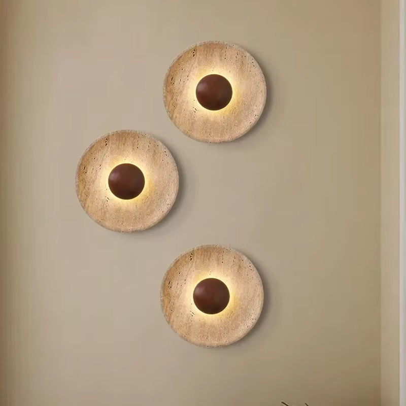 Three stone disc wall sconces with dark wood centers grouped on a beige wall.