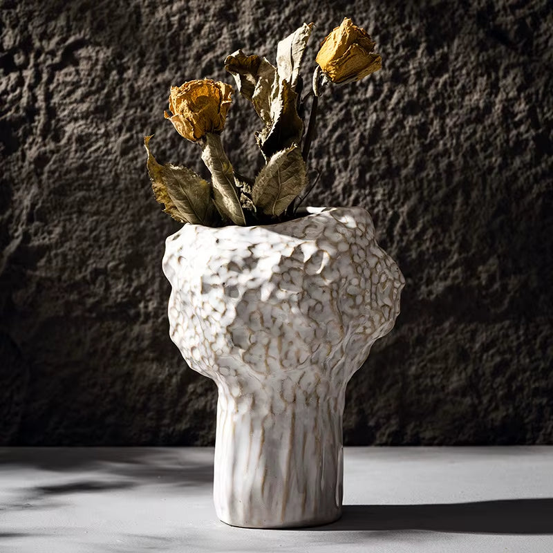 Tall hammered ceramic vase in matte white holding dried roses.