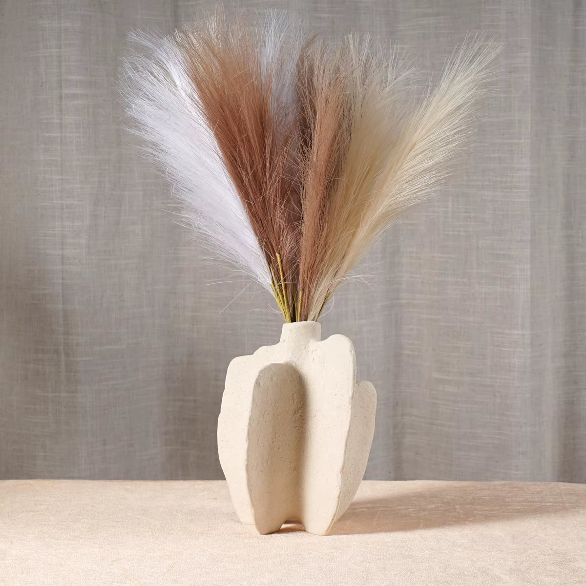 White sculptural ceramic vase with dried pampas grass on a pale tabletop.