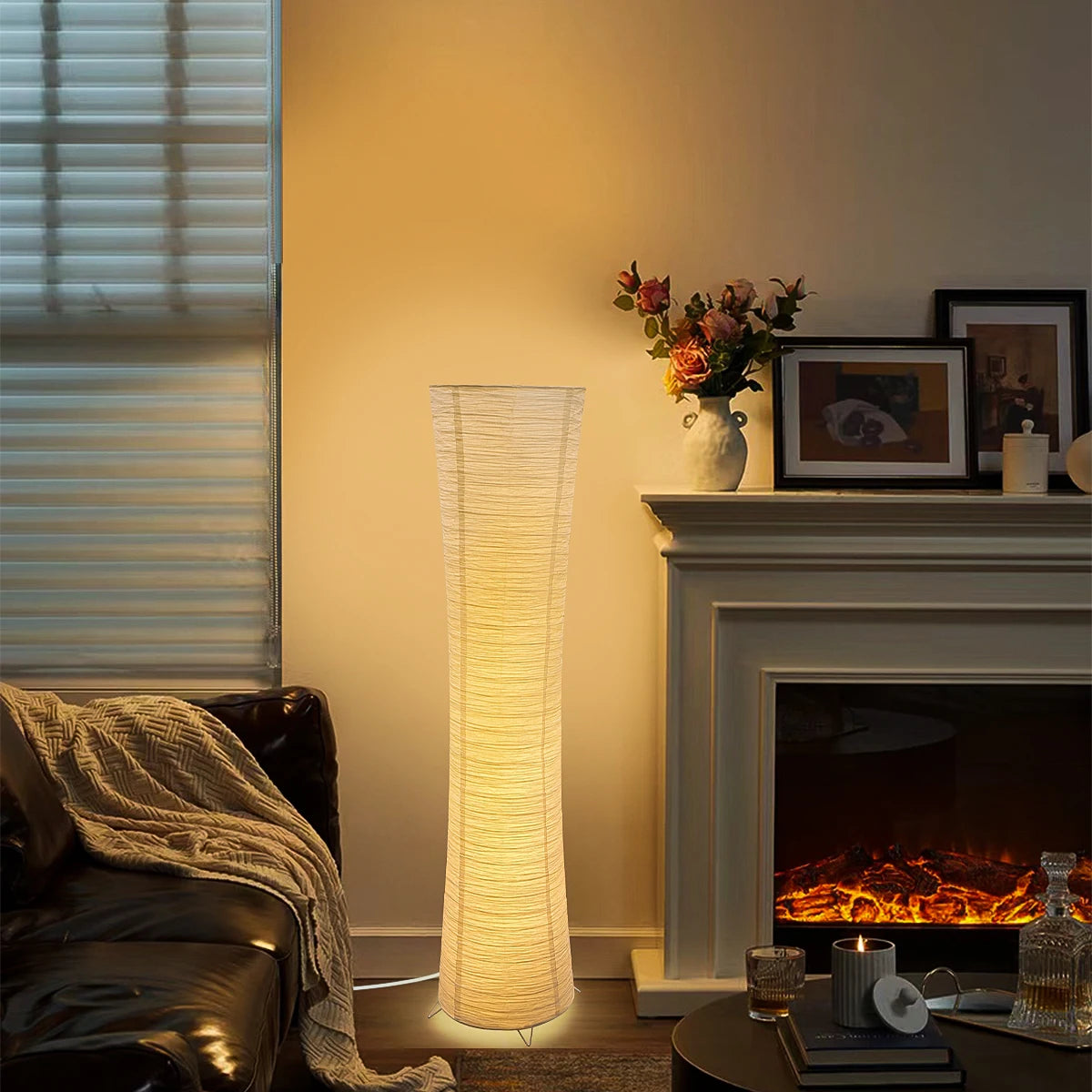 Rice paper column floor lamp lit beside a fireplace in a living room.