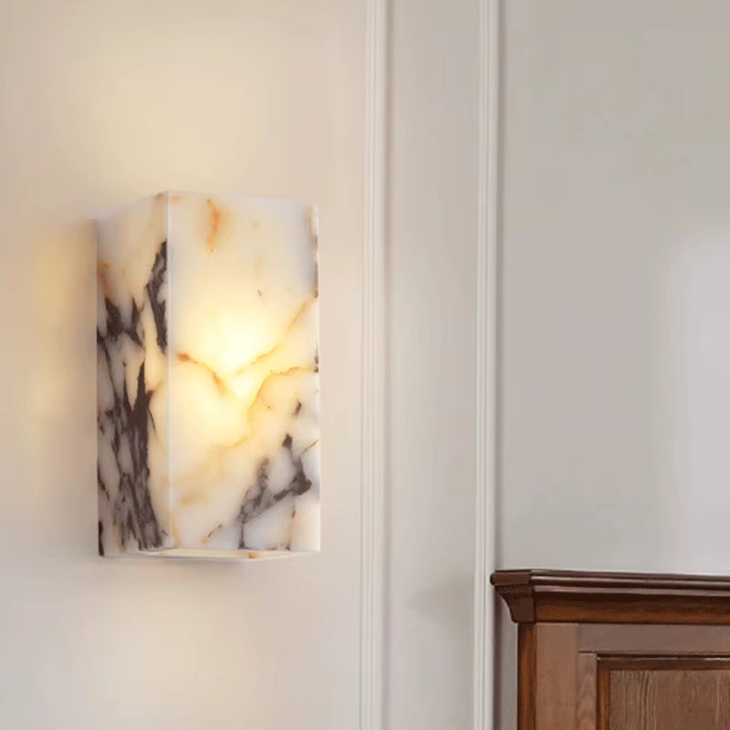 Stone block wall sconce, lit, on a panelled wall above a wood cabinet.