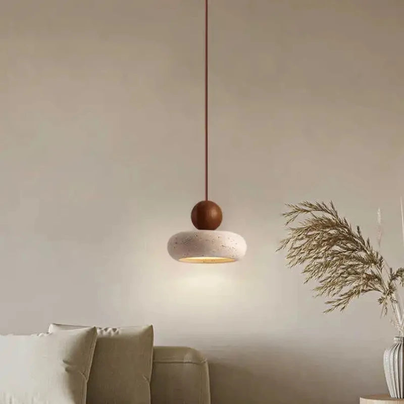 Walnut-color pendant light with a rounded stone shade lit above a beige sofa.