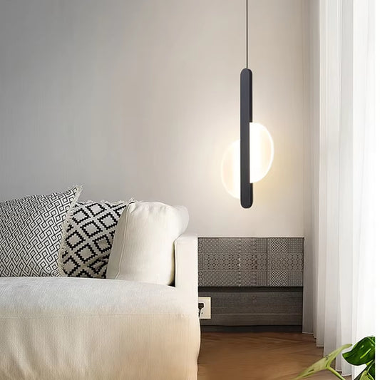 Black bar pendant light with a split round disc, lit, hanging beside a white sofa.