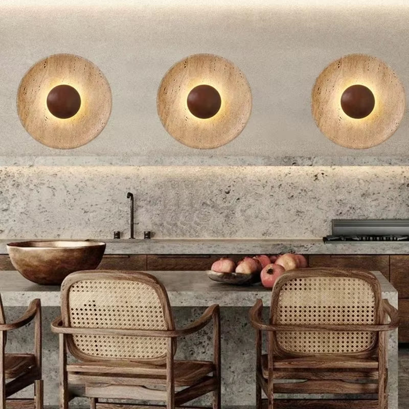 Three stone disc wall sconces with dark wood centers in a row on a plaster wall above a stone counter.