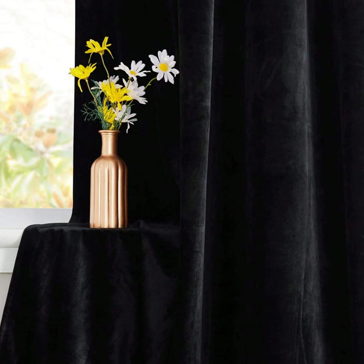 Black velvet curtain falling in heavy folds beside a vase of flowers.