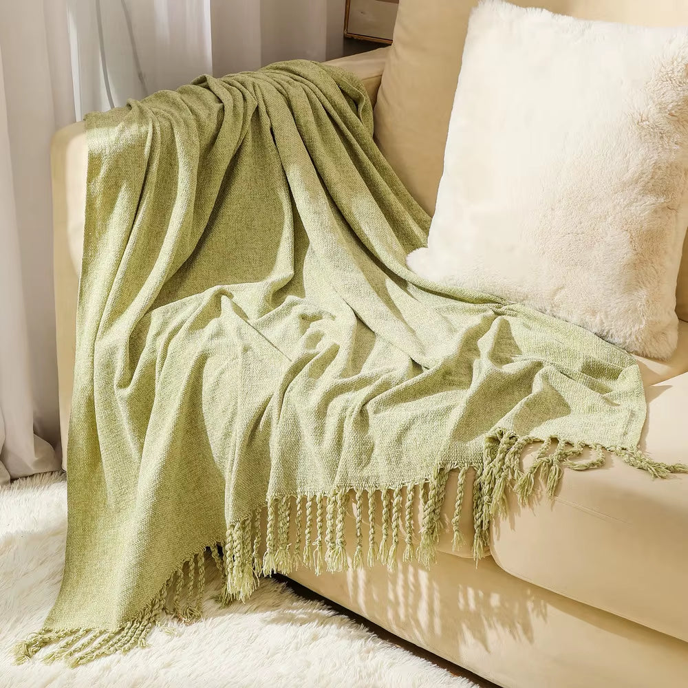 Matcha green chenille throw blanket with knotted fringe draped over a cream sofa.