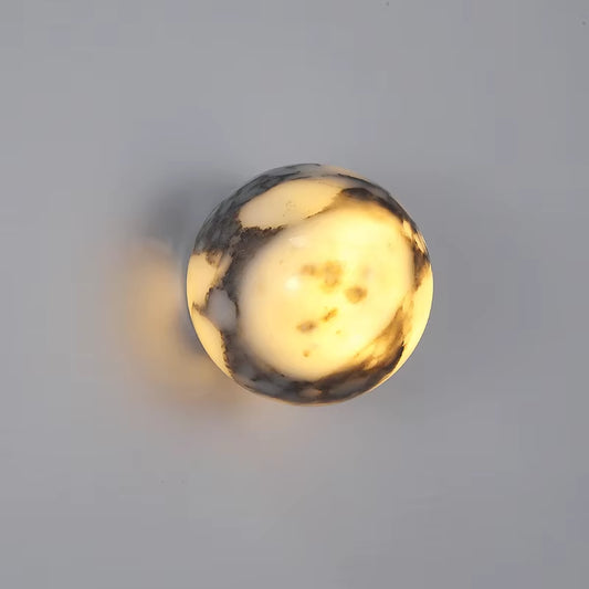 Marble sphere wall sconce, lit, on a gray wall.